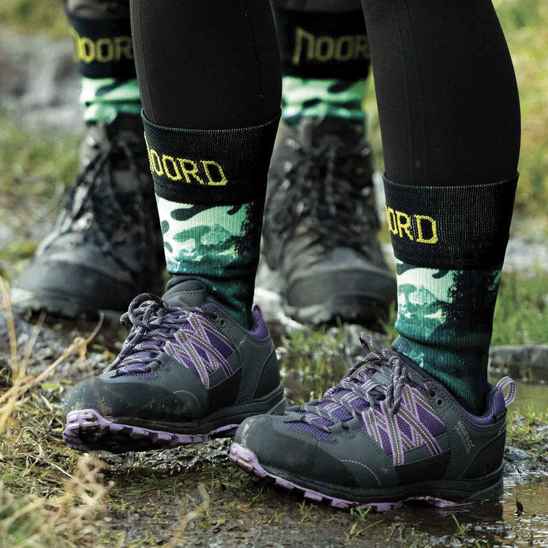 Load image into Gallery viewer, two people wearing waterproof socks with green camouflage pattern and 'NOORD' branding, standing on a natural ground.