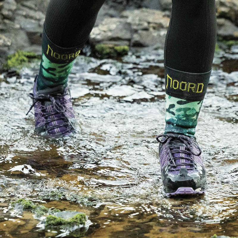 Load image into Gallery viewer, Person wearing waterproof socks, they are green camouflage waterproof socks with 'Noord' branding, walking through a stream.