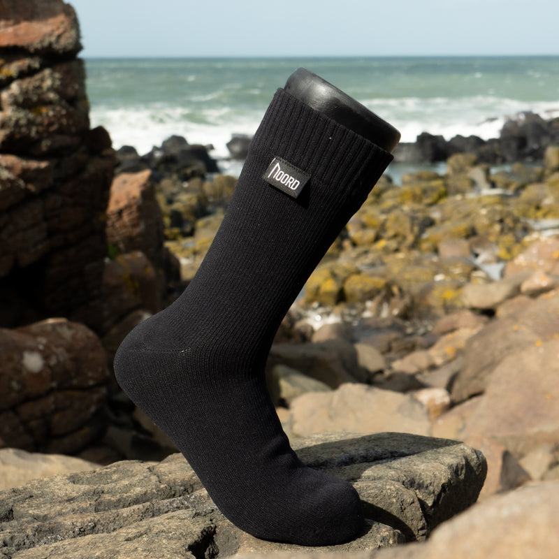 Load image into Gallery viewer, waterproof sock , crew length with a brand logo tag by Noord on a rocky beach
